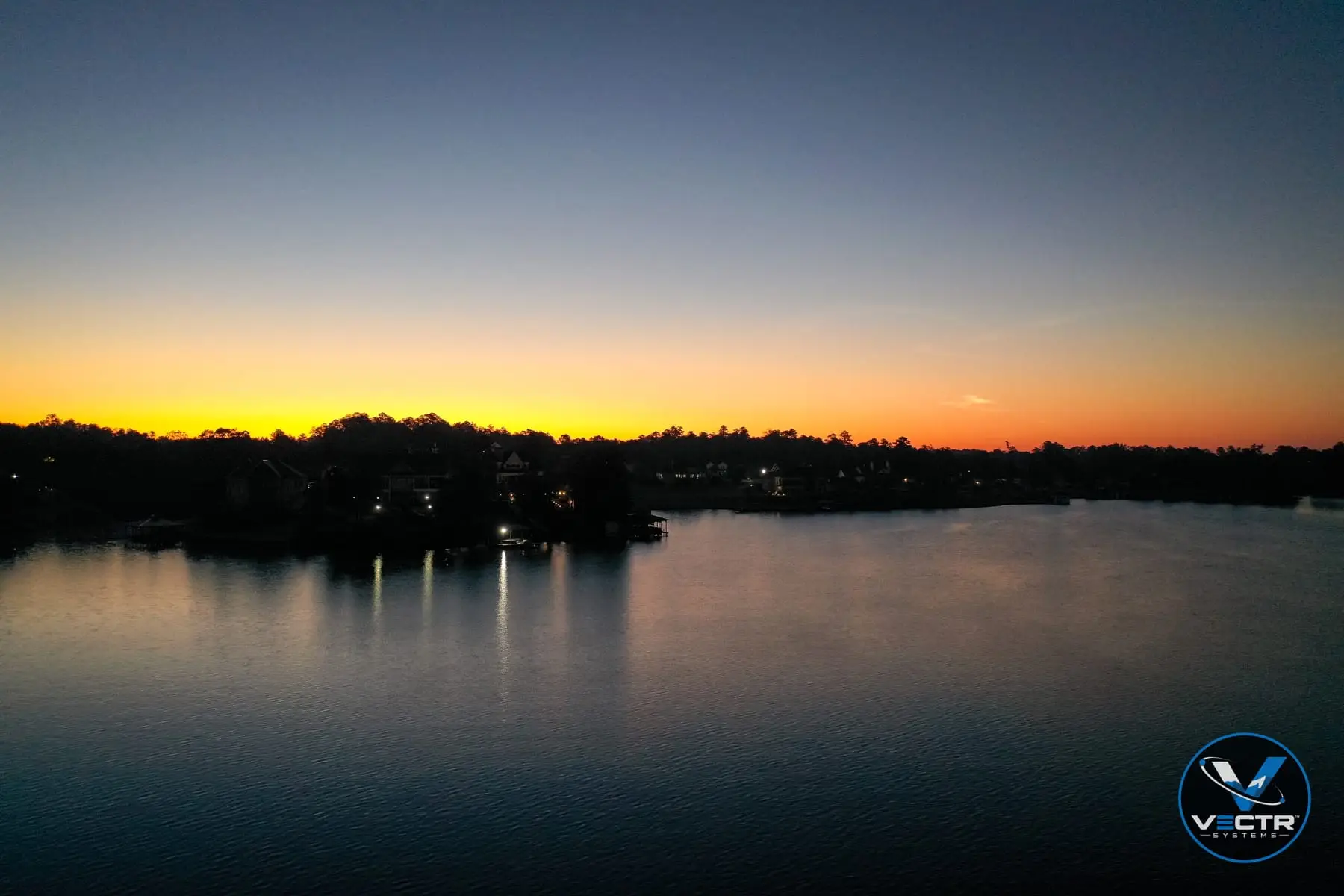 Twilight aerial of lakefront homes with lights reflecting on the water