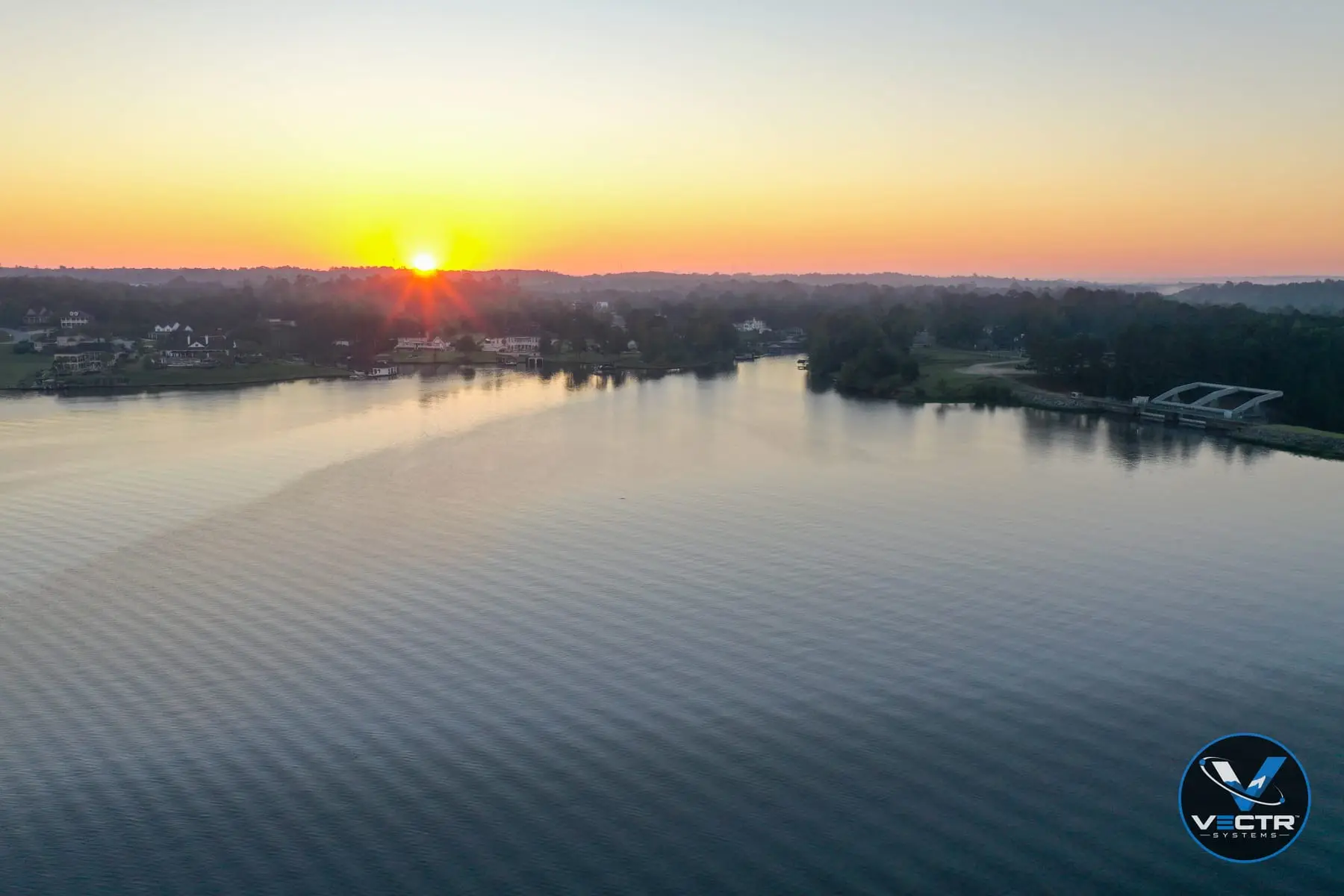 Wide aerial of a lake at sunrise with the sun just above the tree line