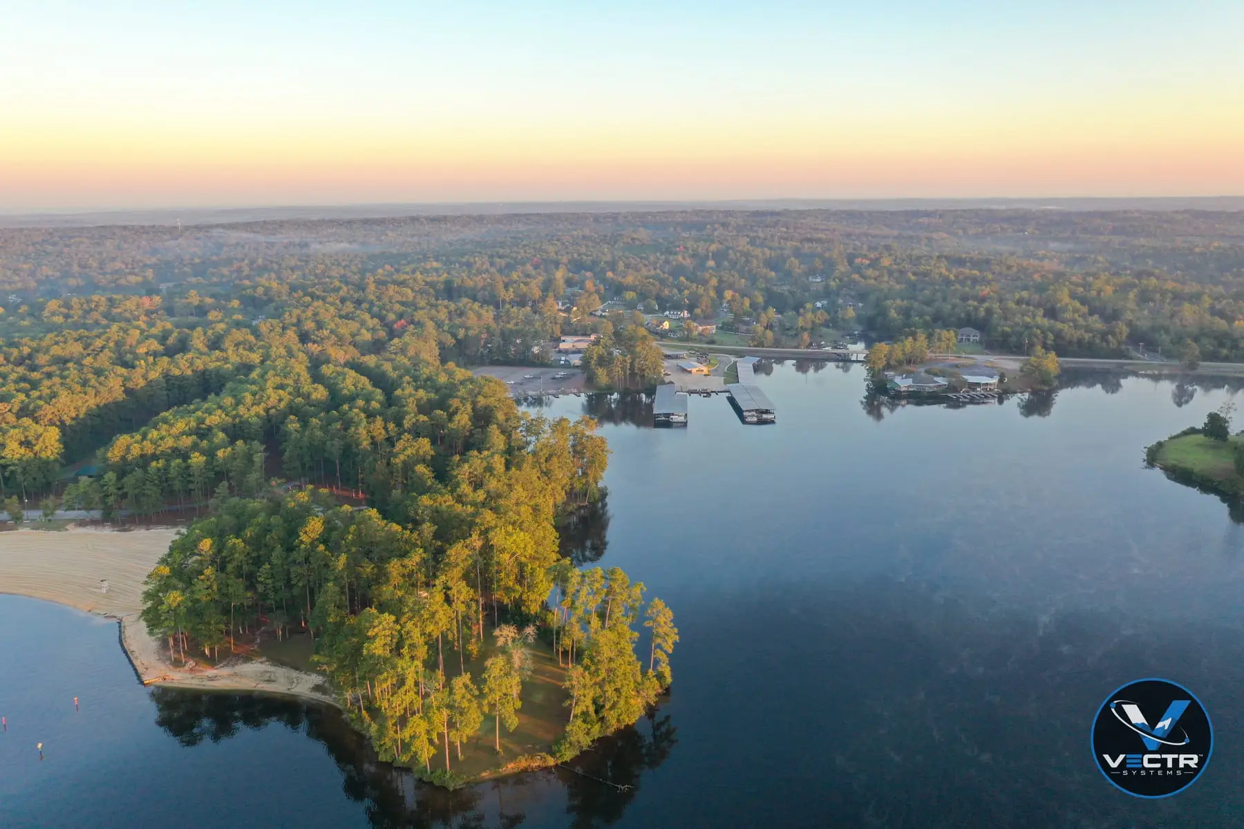 Aerial view of a wooded peninsula, beach, and marina on a lake